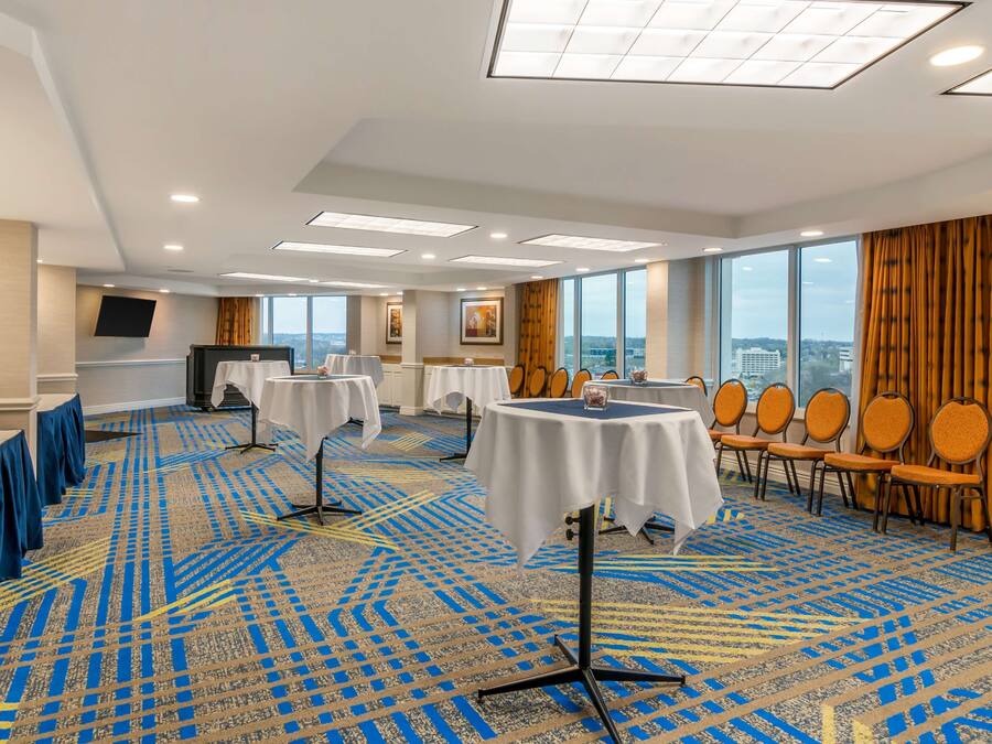Un salón de conferencias de hotel con alfombra estampada, mesas con manteles blancos y sillas.