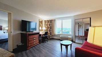A hotel room with a bed, a TV, a desk with a chair, a small table, and a red sofa.