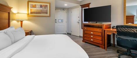 Une chambre d’hôtel avec un grand lit, un bureau avec une chaise, une télévision et une porte donnant sur une autre pièce.