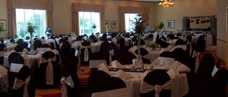 A banquet hall with round tables, black chairs with white sashes, and chandeliers.
