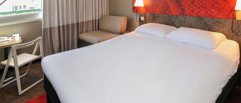 A hotel room with a bed, a chair, a desk, and a view of the outside.