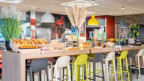 A modern bar area with a wooden counter, colorful chairs, and various food items displayed. - ibis Lyon Villefranche sur Saone (Limas)