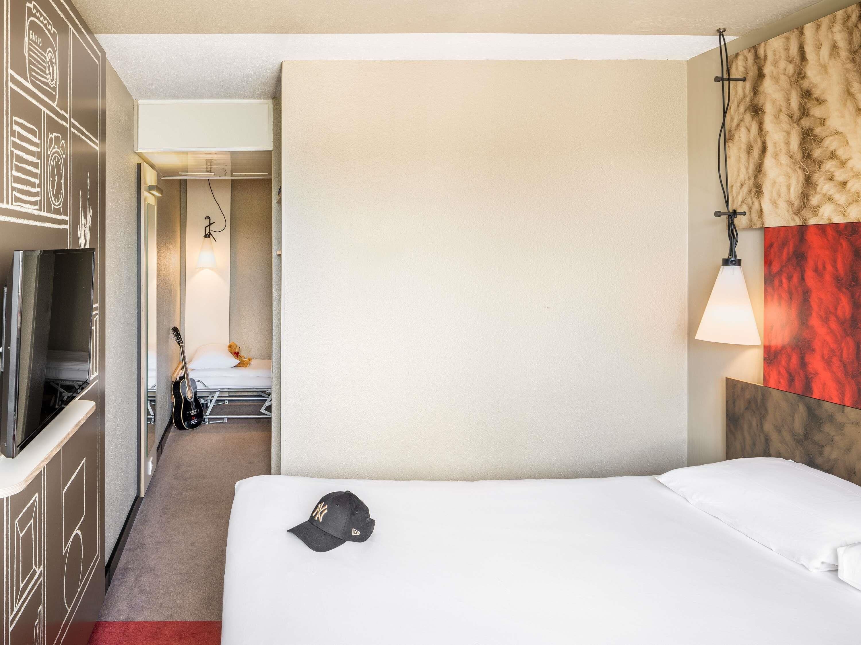 Une chambre d’hôtel avec un lit, une télévision, une guitare et un ours en peluche.