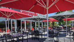 An outdoor dining area with red umbrellas, tables, and chairs. - ibis Lyon Villefranche sur Saone (Limas)