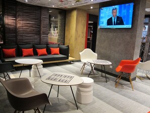 A modern lounge area with a sofa, chairs, and a TV screen displaying a news program. - ibis Lyon Villefranche sur Saone (Limas)