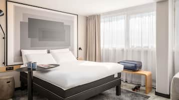 Una habitación de hotel moderna con una cama grande, una mesita de noche, una lámpara y una ventana con cortinas.