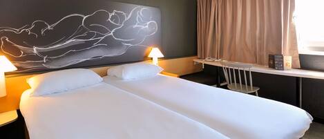 Una habitación de hotel con cama, lámparas de noche, un escritorio con teléfono y una ventana con cortinas.