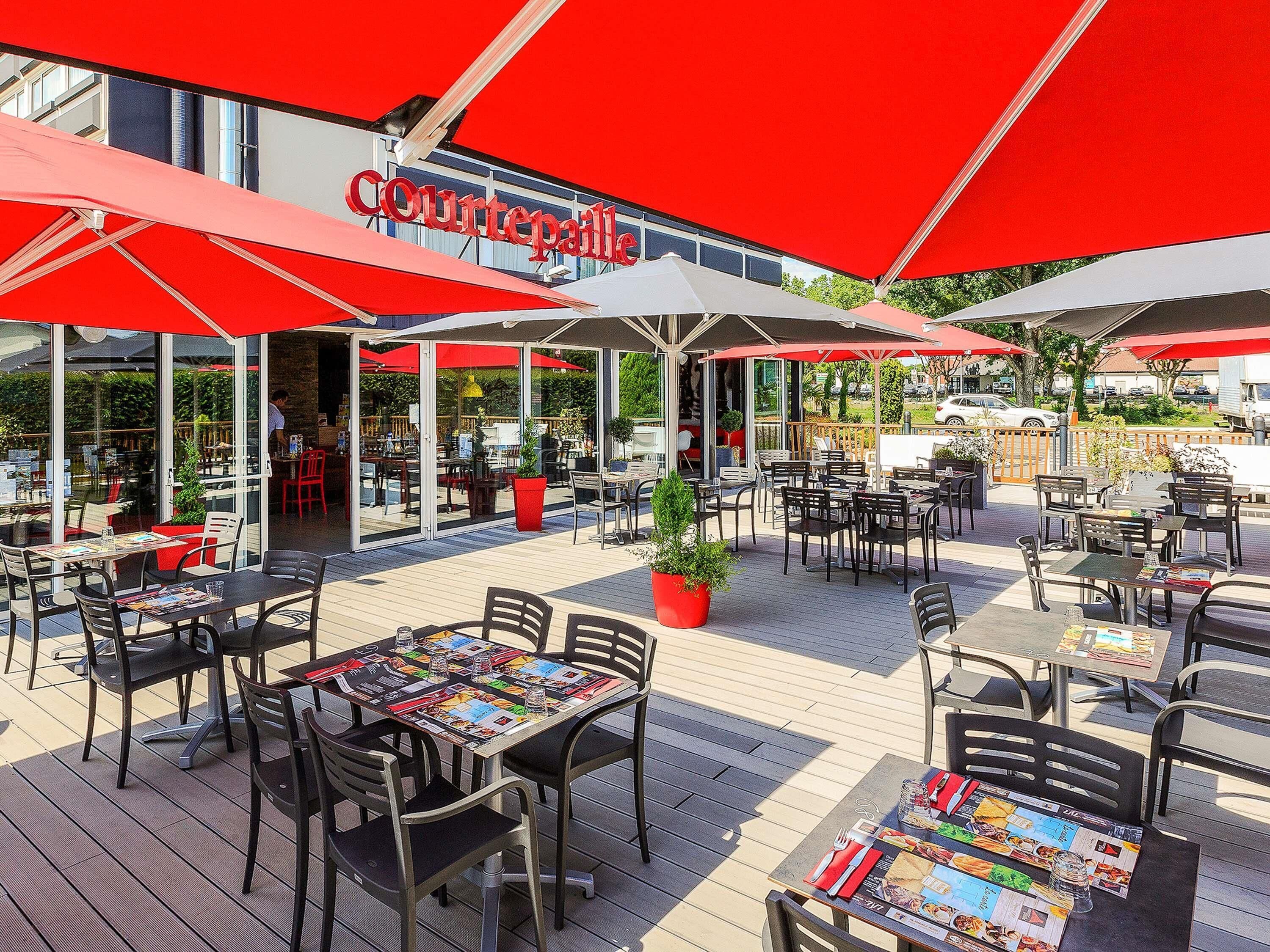 Ein Straßencafé mit roten Sonnenschirmen, Tischen und Stühlen.