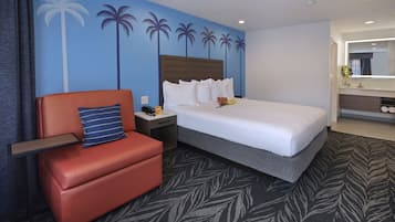 A hotel room with a bed, a nightstand, a red chair, a blue pillow, and a wall with palm tree decals.