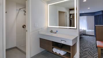 Une salle de bain moderne avec un grand miroir, une douche, un lavabo avec un porte-serviettes et un meuble-lavabo en bois.