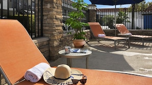 A sunlit outdoor seating area with lounge chairs, a table with a plant, and a blue umbrella. - Tropicana Inn and Suites (Anaheim)