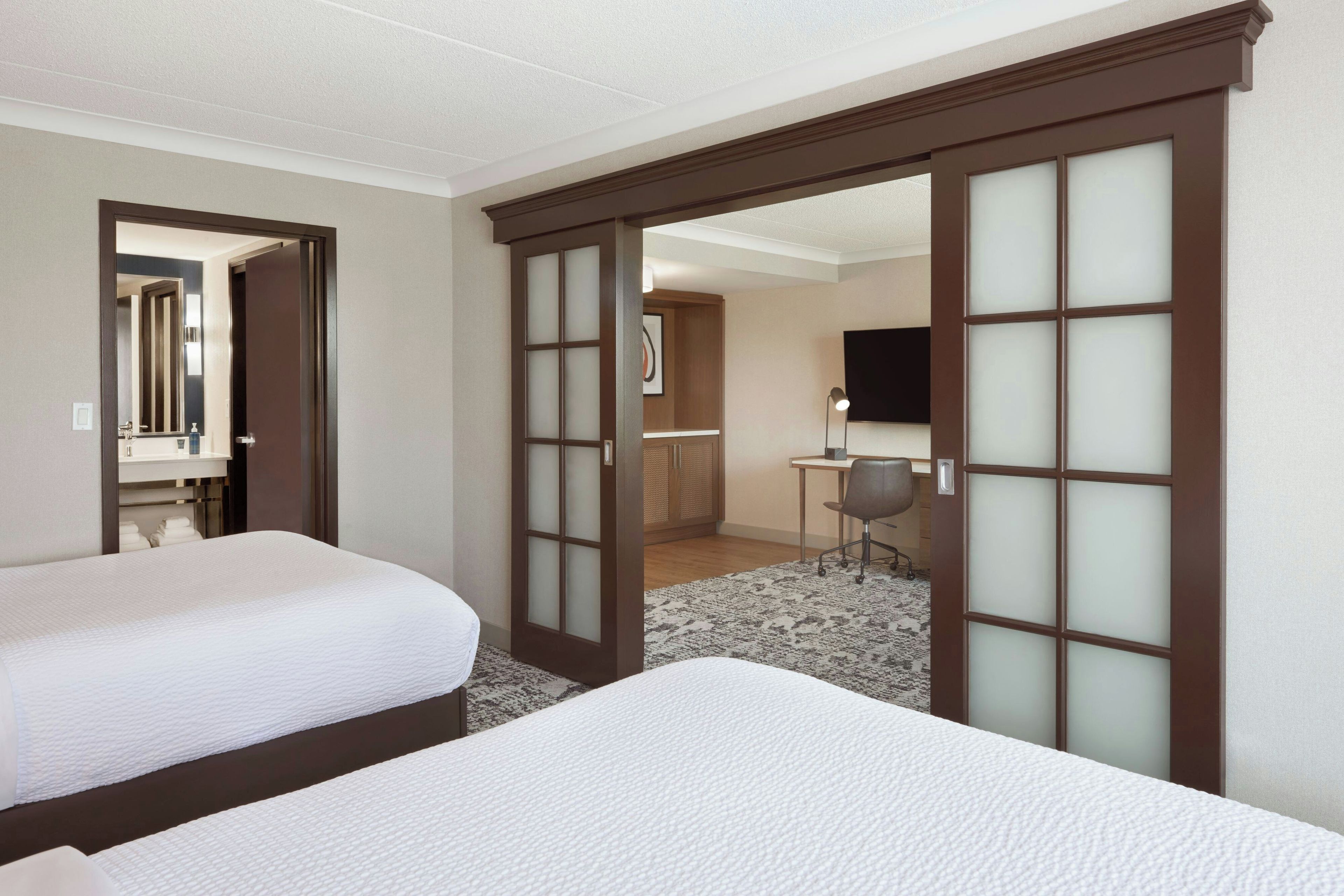 A hotel room with two beds, a desk, a chair, and a TV.