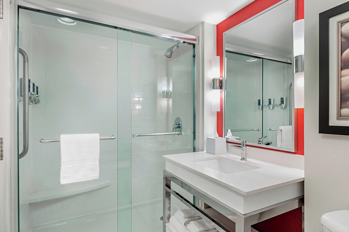 Une salle de bain moderne avec une douche à parois de verre, un lavabo blanc et un grand miroir avec un cadre rouge.