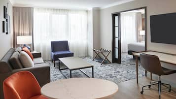 A hotel room with a sofa, armchair, small table, desk, and a bed.