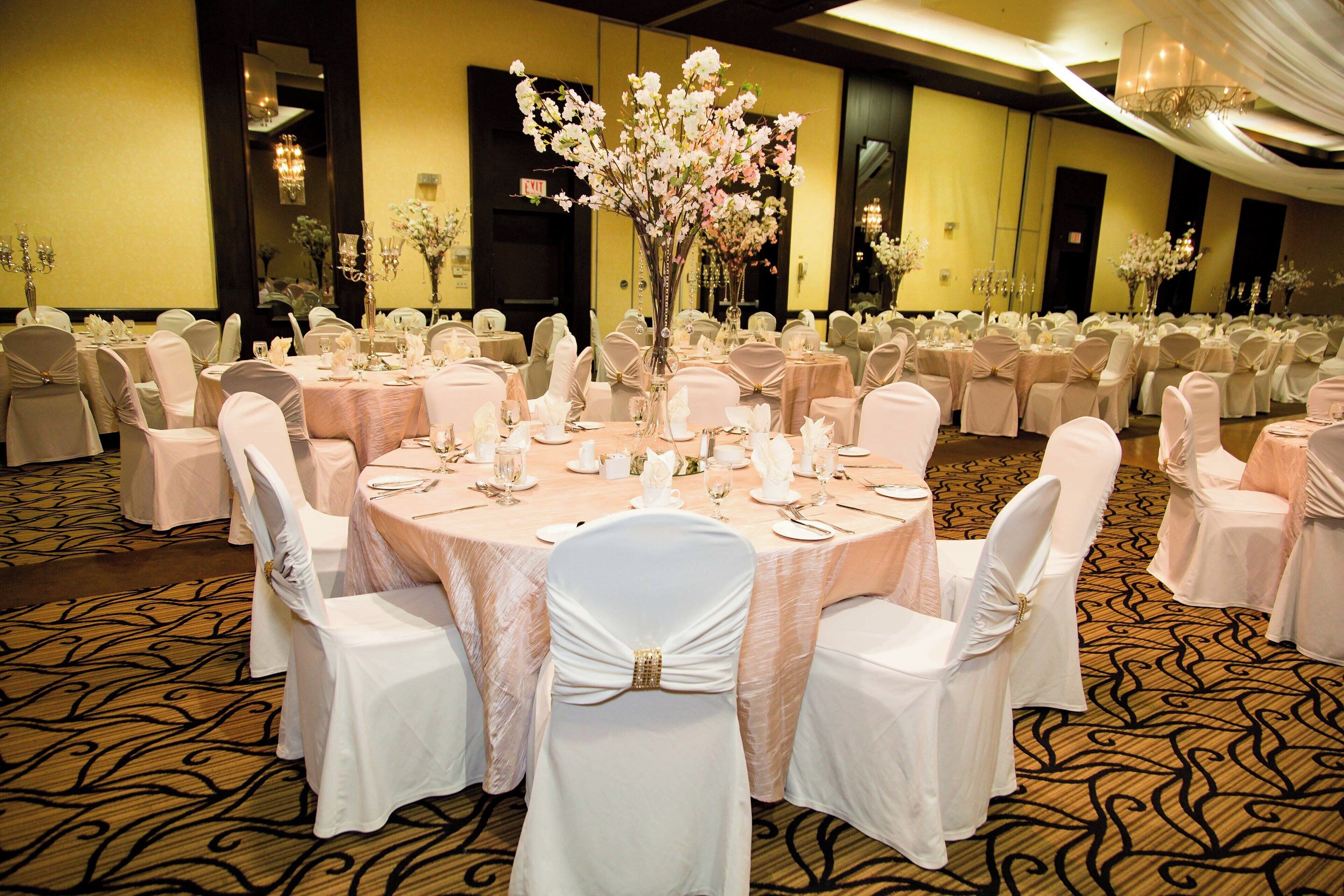 Un salón de banquetes con mesas redondas, sillas blancas y centros de mesa florales.