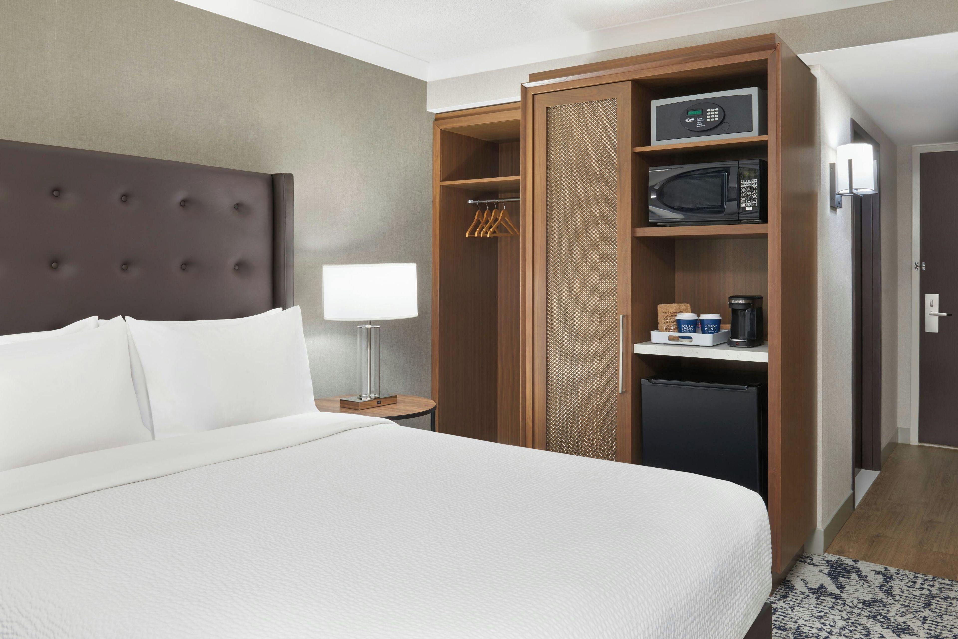 A hotel room with a large bed, a wardrobe, a microwave, and a coffee machine.