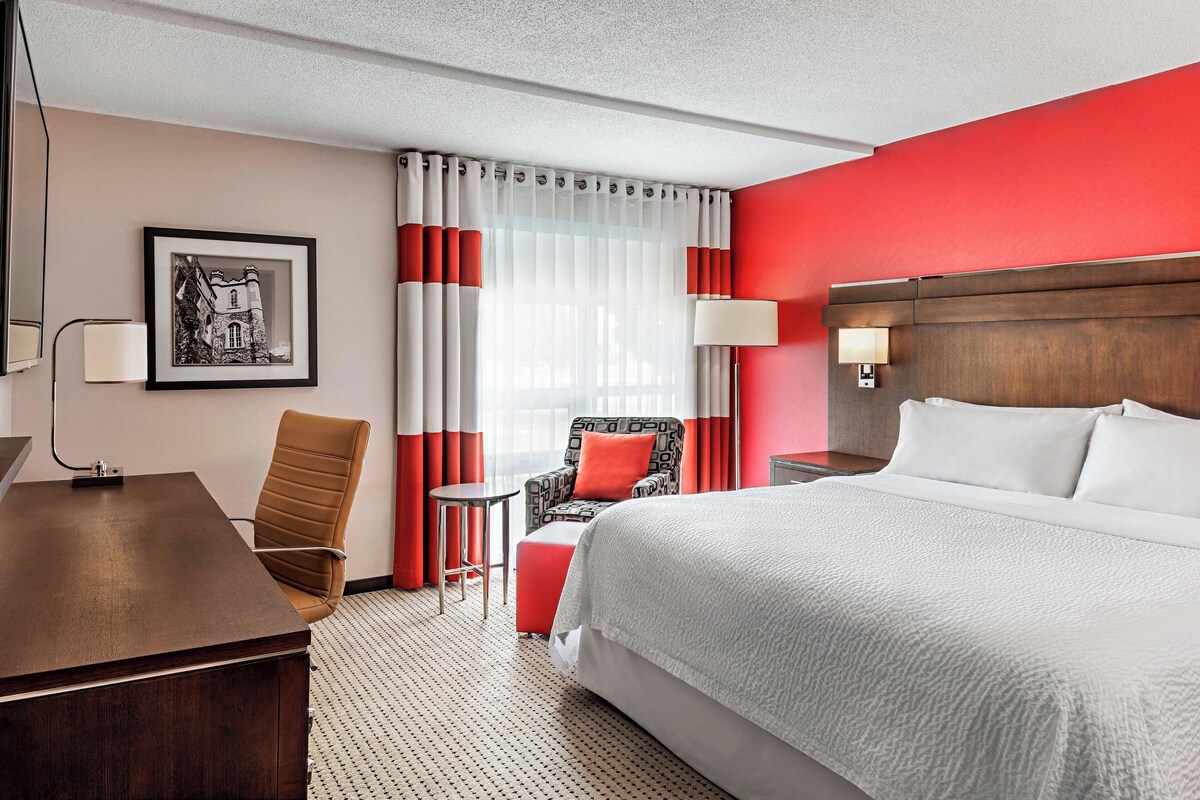 Une chambre d’hôtel avec un grand lit, un bureau, une chaise, une petite table et une lampe.