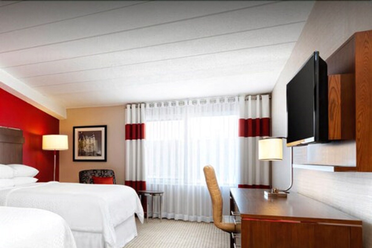 Une chambre d’hôtel avec deux lits, un bureau, une chaise, une télévision et une fenêtre avec des rideaux.