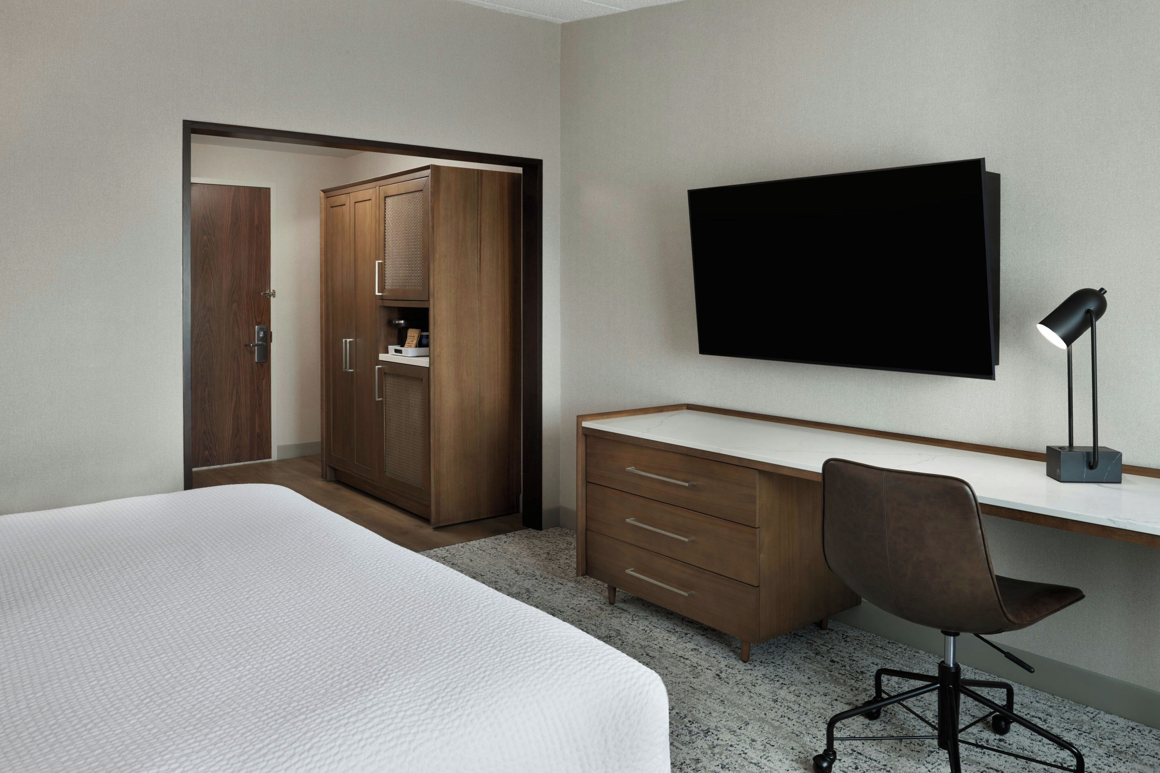 Une chambre d’hôtel comprenant un lit, un bureau, une chaise, une armoire et un téléviseur.