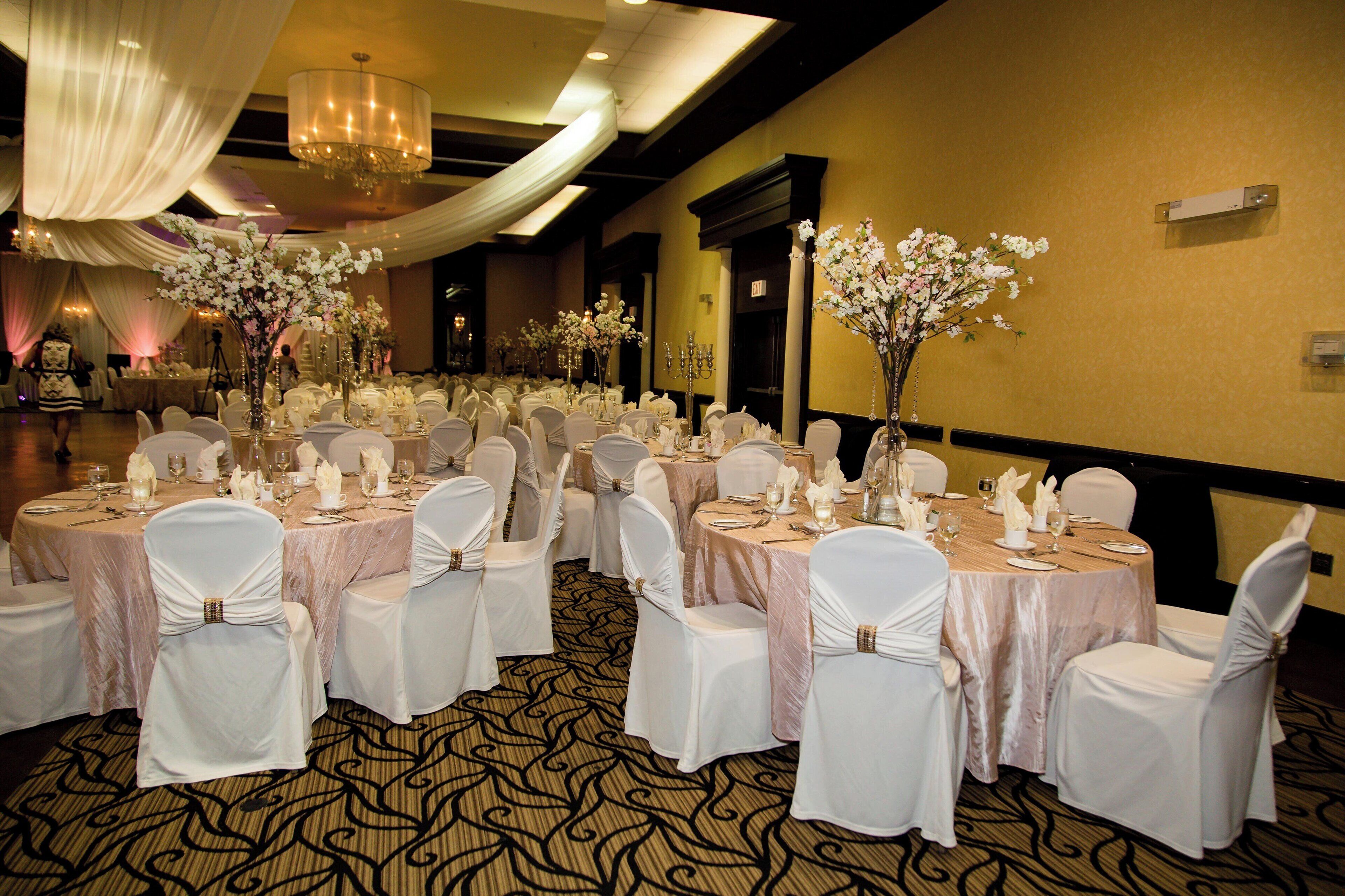 A banquet hall with round tables set for a formal event, featuring white tablecloths and chairs with white sashes.