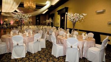 A banquet hall with round tables set for a formal event, featuring white tablecloths and chairs with white sashes.