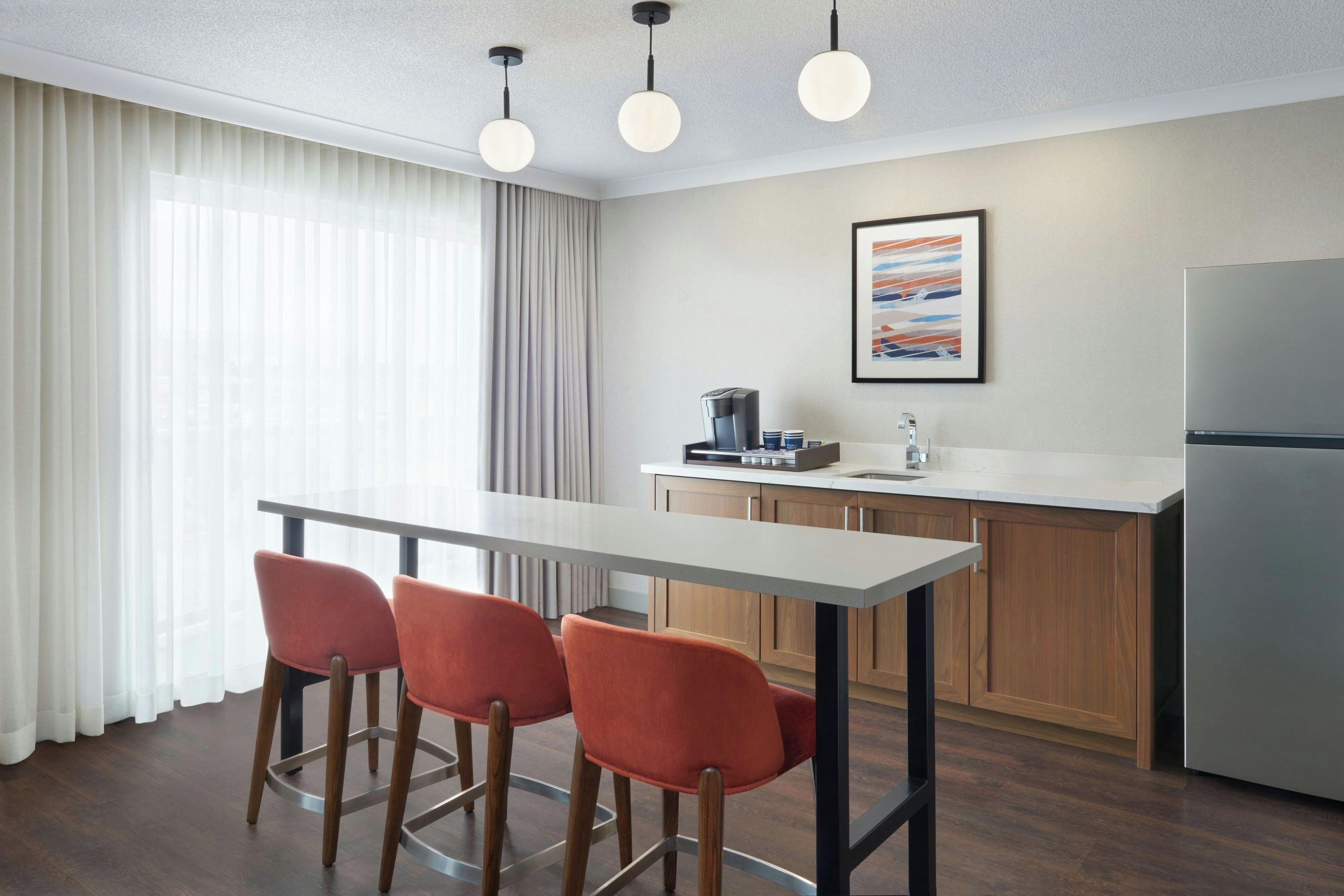 A modern kitchen with a bar area, a coffee machine, and a refrigerator.