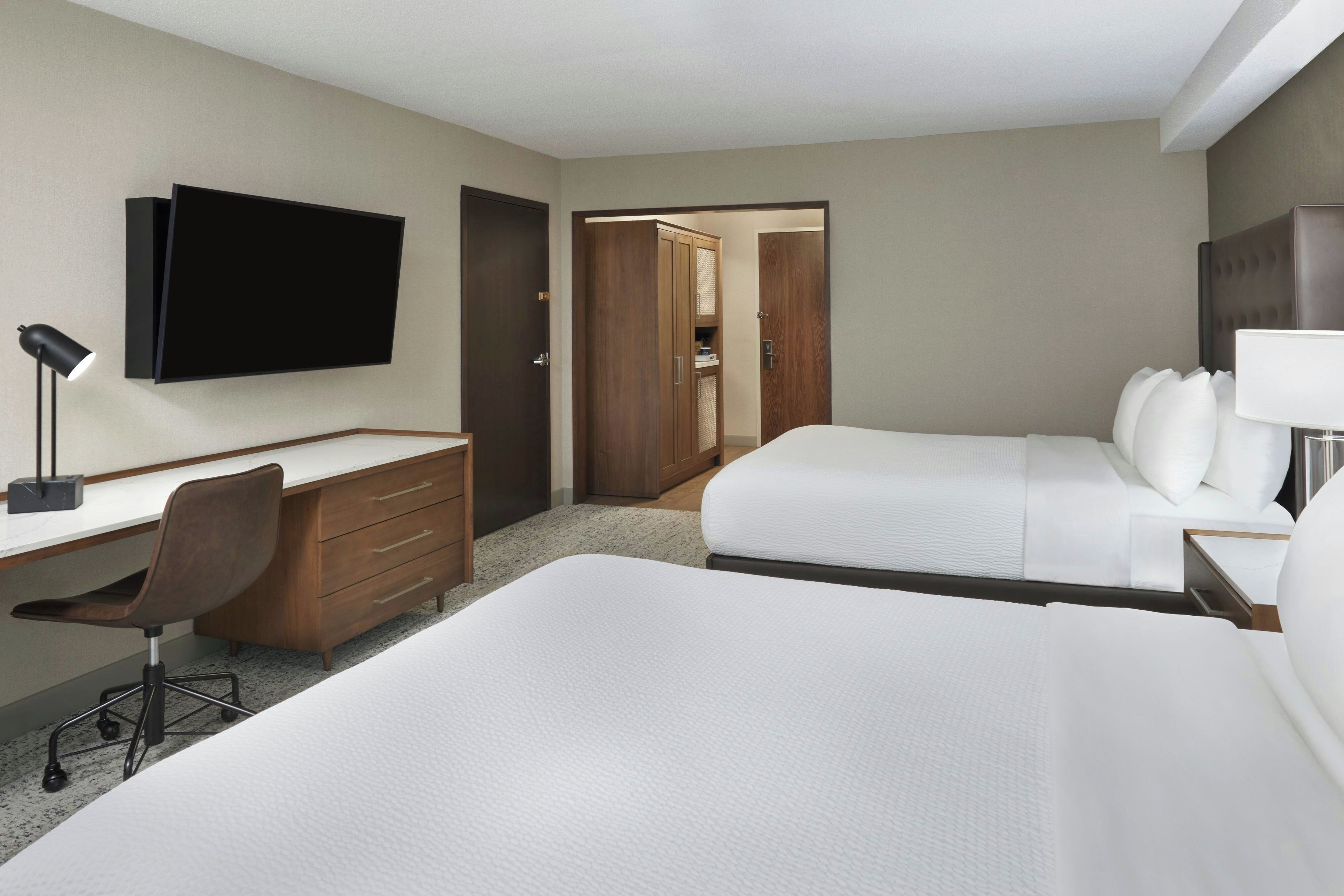 Una habitación de hotel con cama, escritorio, silla, televisión y armario.