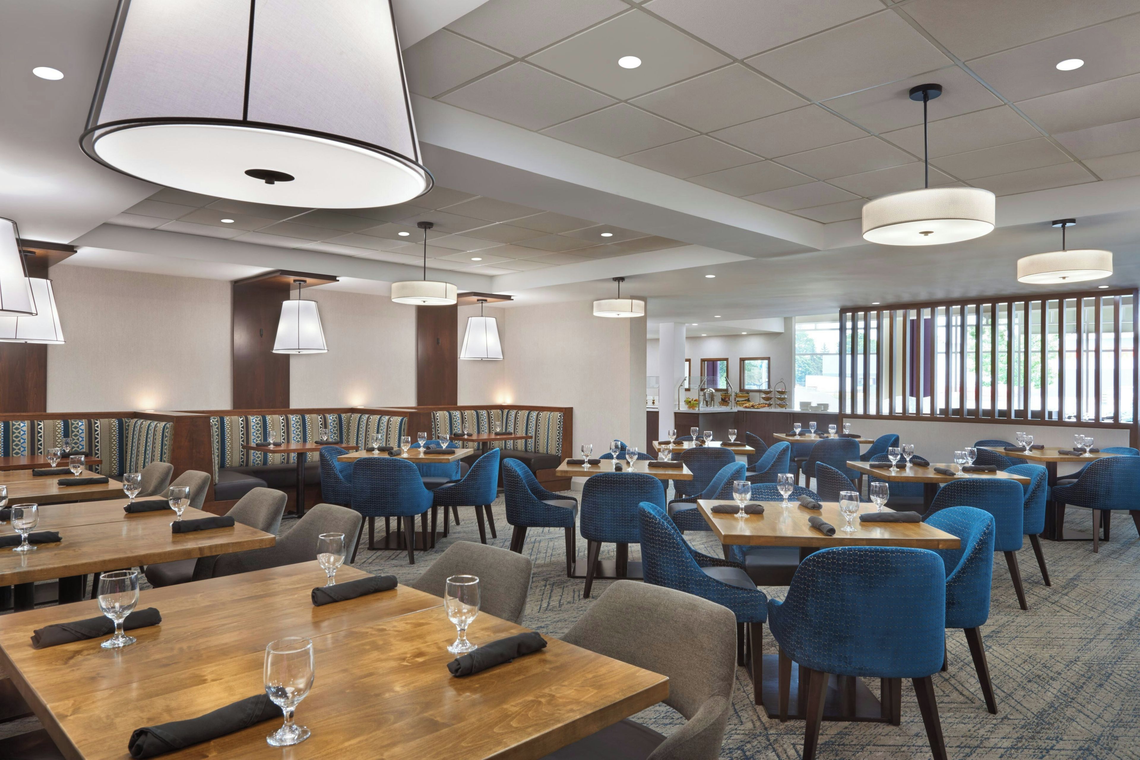 A hotel dining area with multiple tables, chairs, and hanging pendant lights.