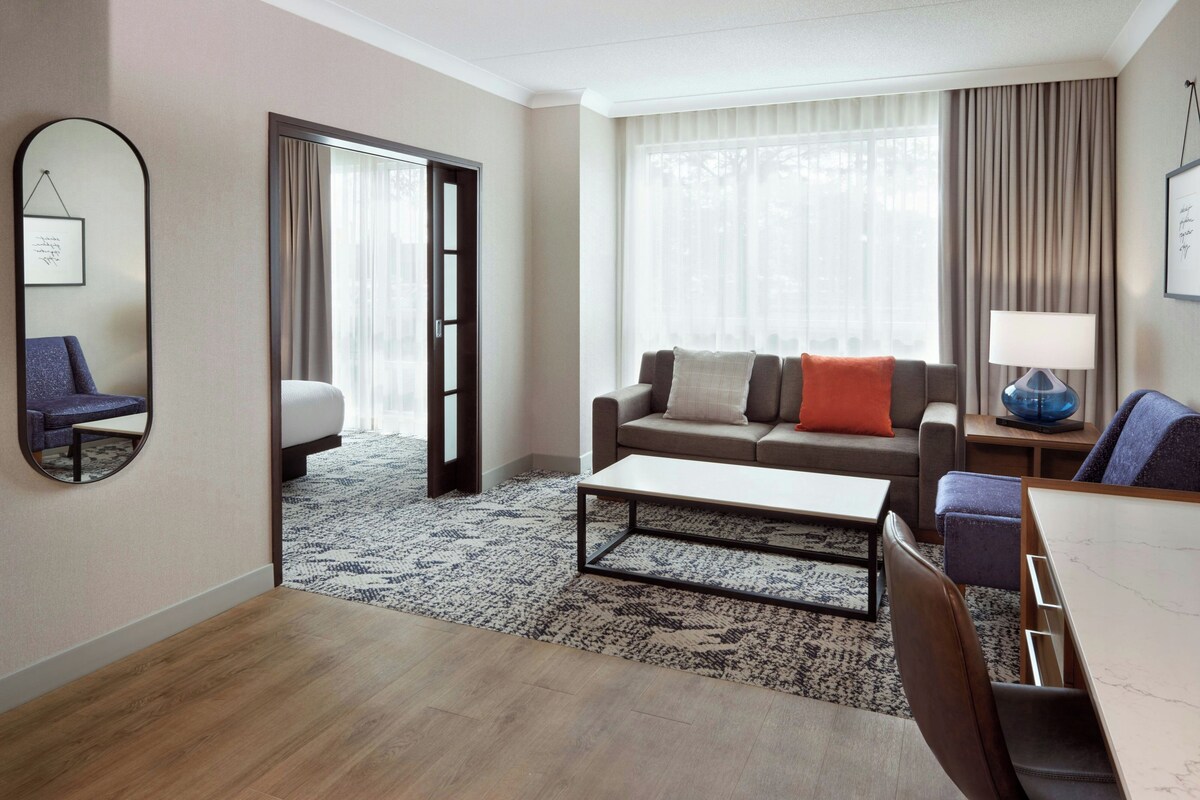 Habitación de hotel con sofá, mesa de centro, silla, lámpara y un espejo grande.
