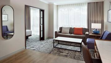 A hotel room with a sofa, a coffee table, a chair, a lamp, and a large mirror.