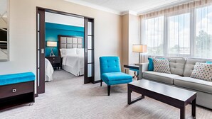 Une chambre d’hôtel avec un lit, un fauteuil bleu, un canapé, une table basse et une grande fenêtre.