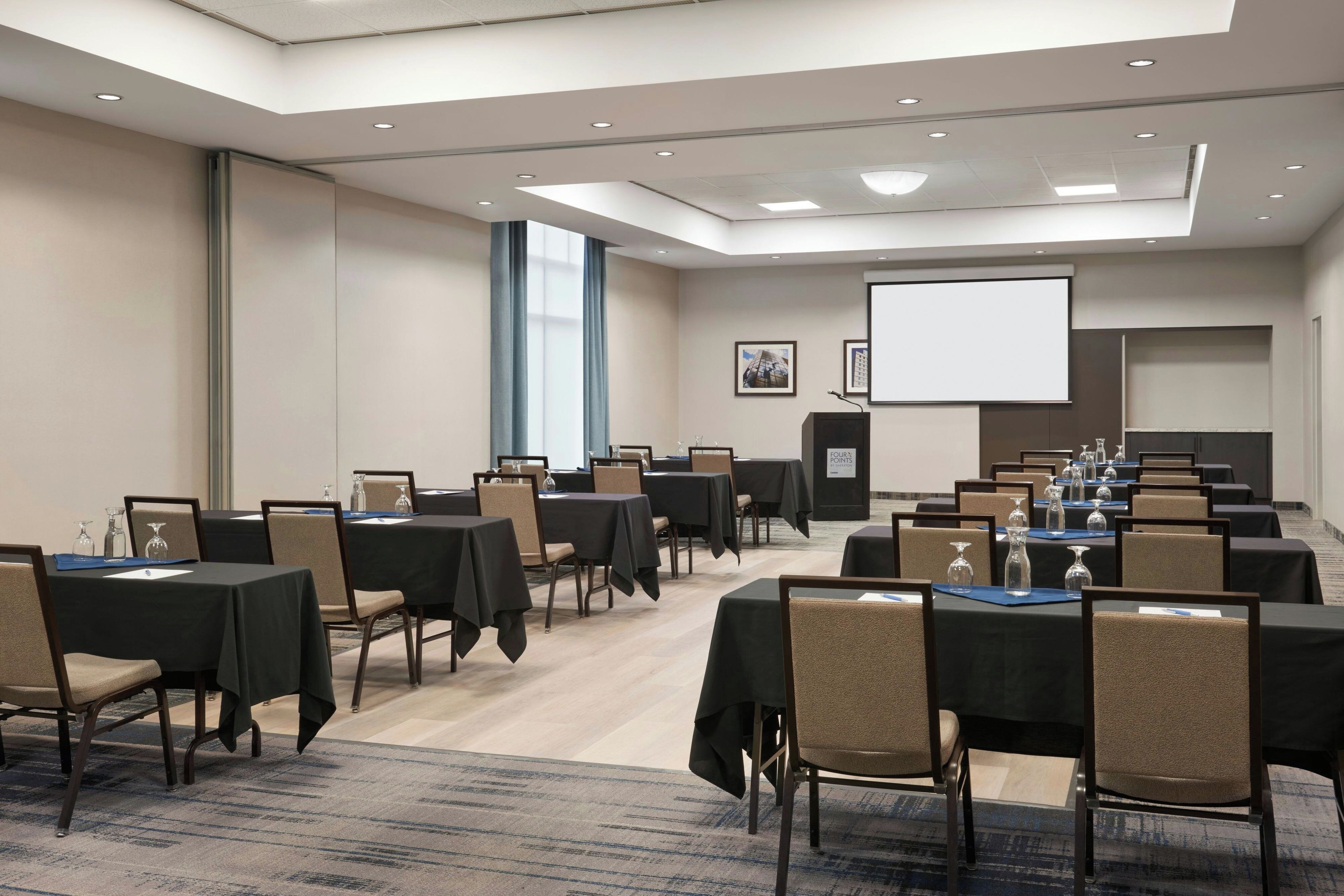 Un salón de conferencias con varias mesas y sillas, una pantalla grande y un proyector.
