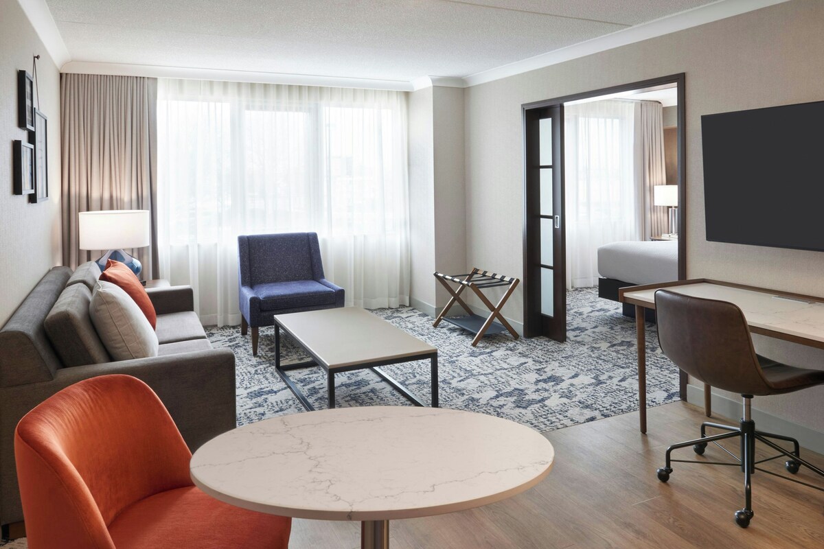 Una habitación de hotel con sofá, sillón, escritorio y una mesita.
