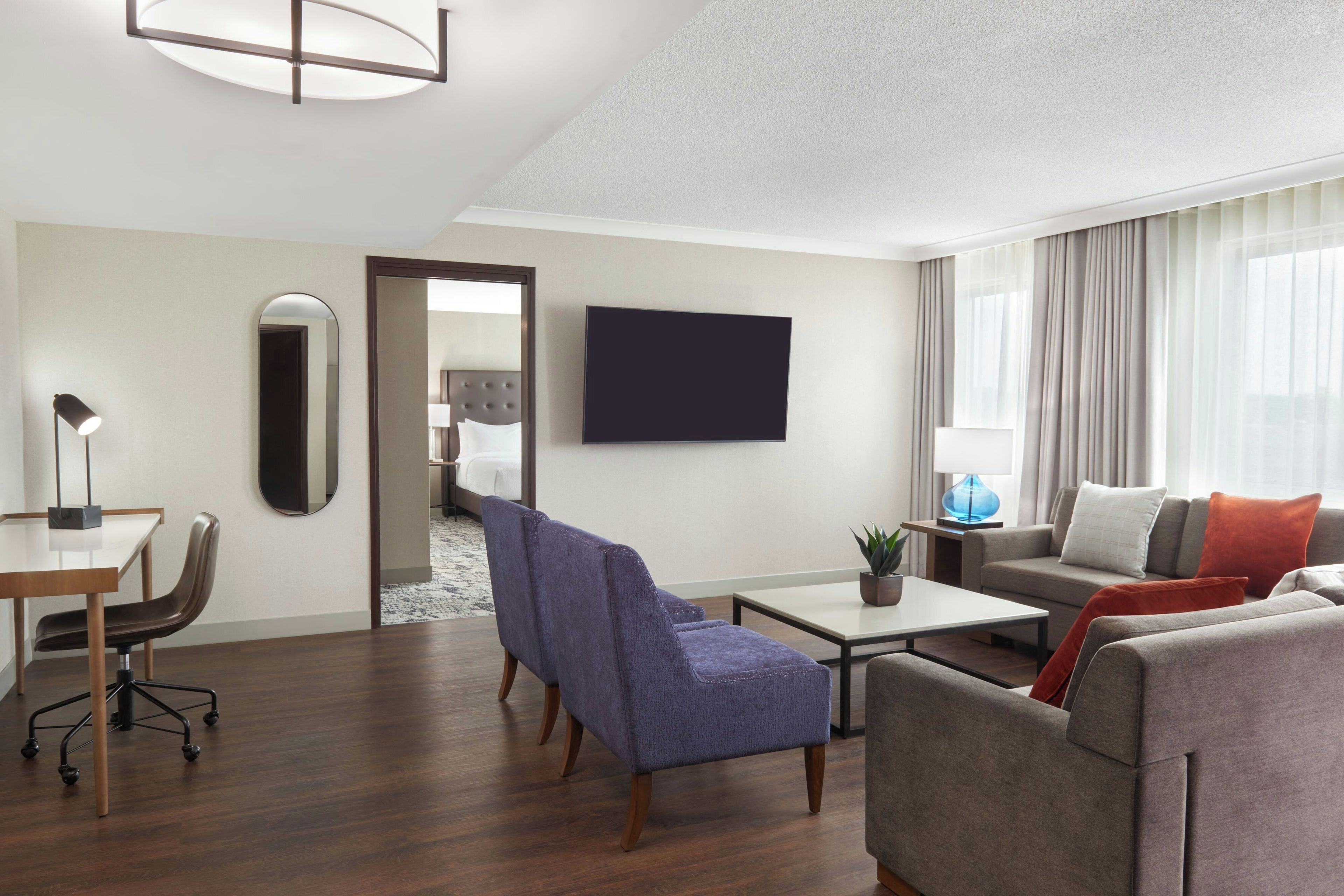 Una habitación de hotel moderna con televisión de pantalla plana, un sofá, una silla, un escritorio y una cama.