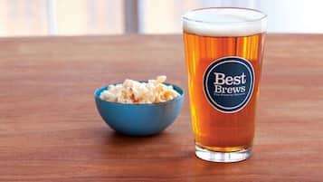 Una cerveza con una etiqueta que dice "Best Brews" junto a un cuenco de palomitas de maíz sobre una mesa de madera.