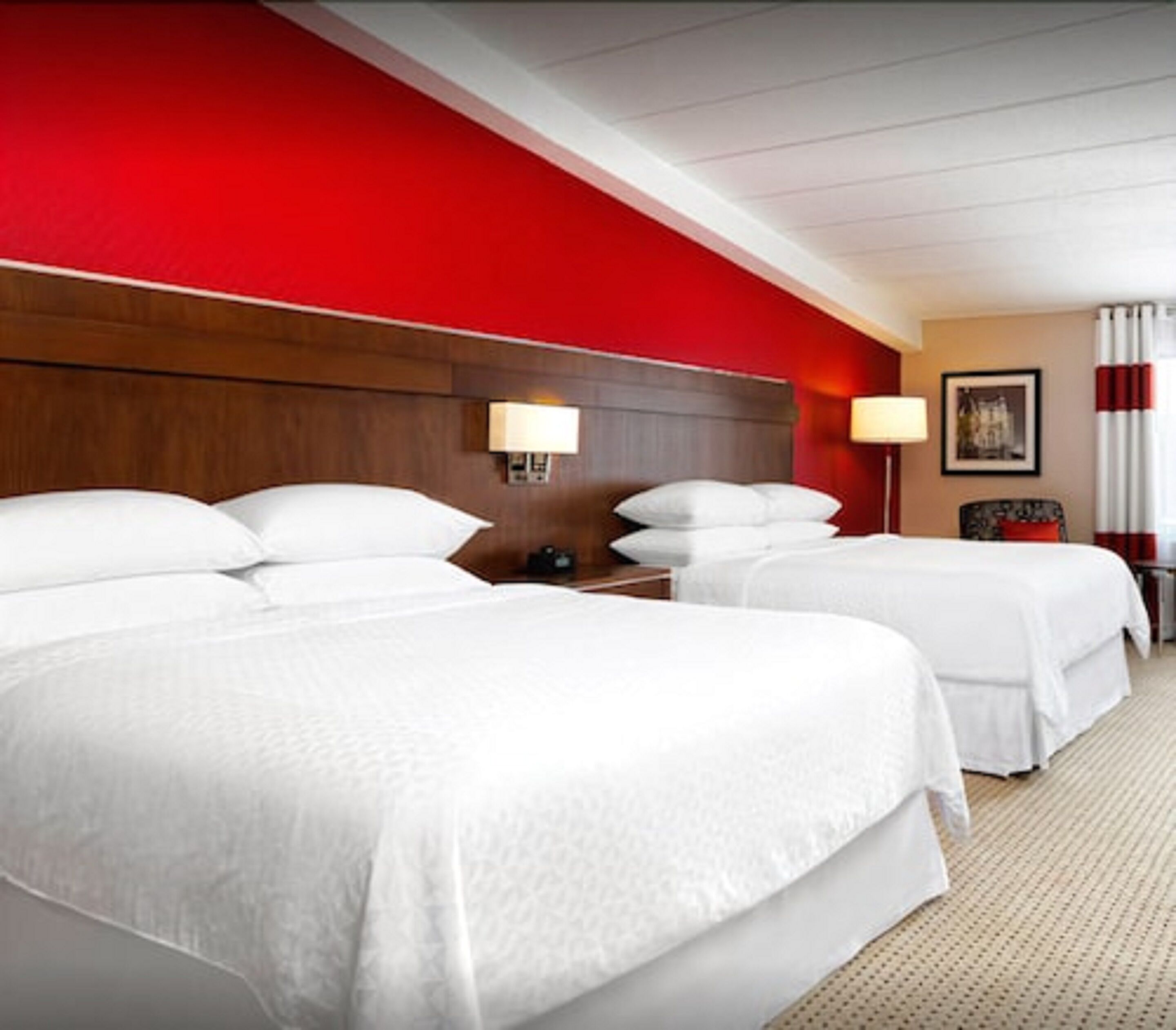 Ein Hotelzimmer mit zwei Betten, einem hölzernen Kopfteil, einem Nachttisch mit Lampe und einem gerahmten Bild an der Wand.
