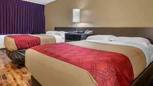A hotel room with two beds, a nightstand with a lamp, and a large window with purple curtains. - Econo Lodge Sebring (Avon Park)