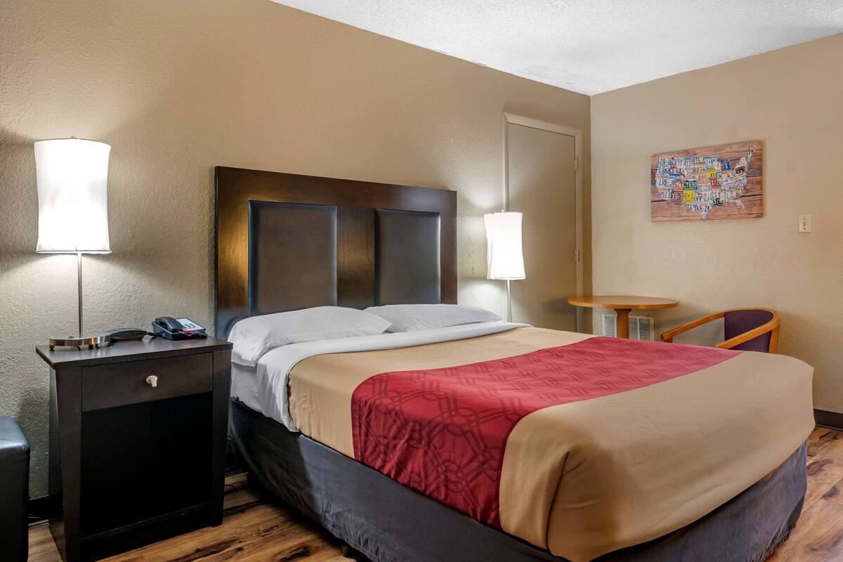 A hotel room with a bed, bedside tables, a small desk, a chair, and a wall map.