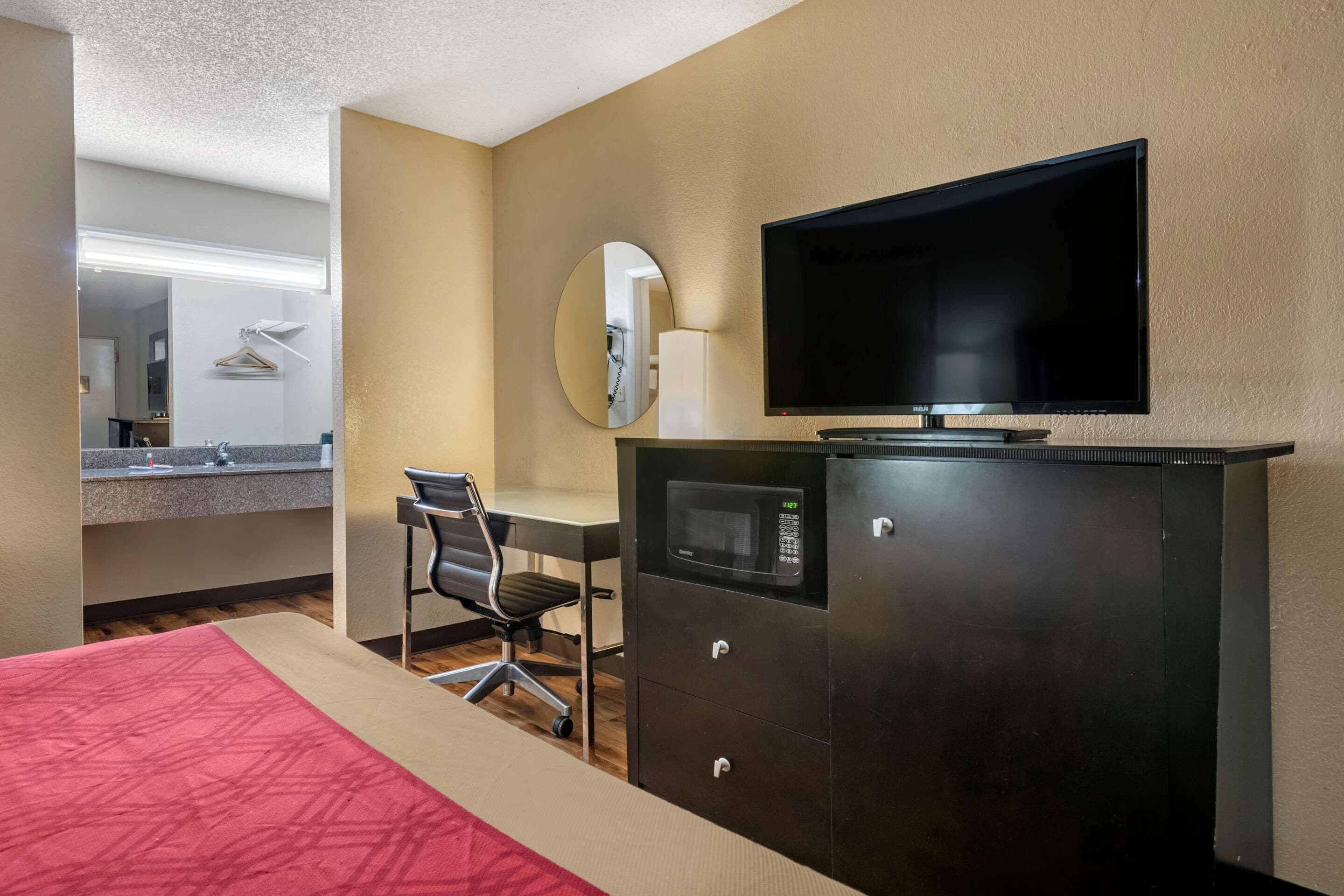 Een hotelkamer met een bed, een bureau met stoel, een flatscreen televisie, een magnetron en een spiegel.