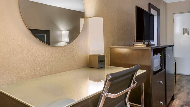 A hotel room with a round mirror, a desk, a chair, a flat-screen TV, a microwave, and a refrigerator. - Econo Lodge Sebring (Avon Park)