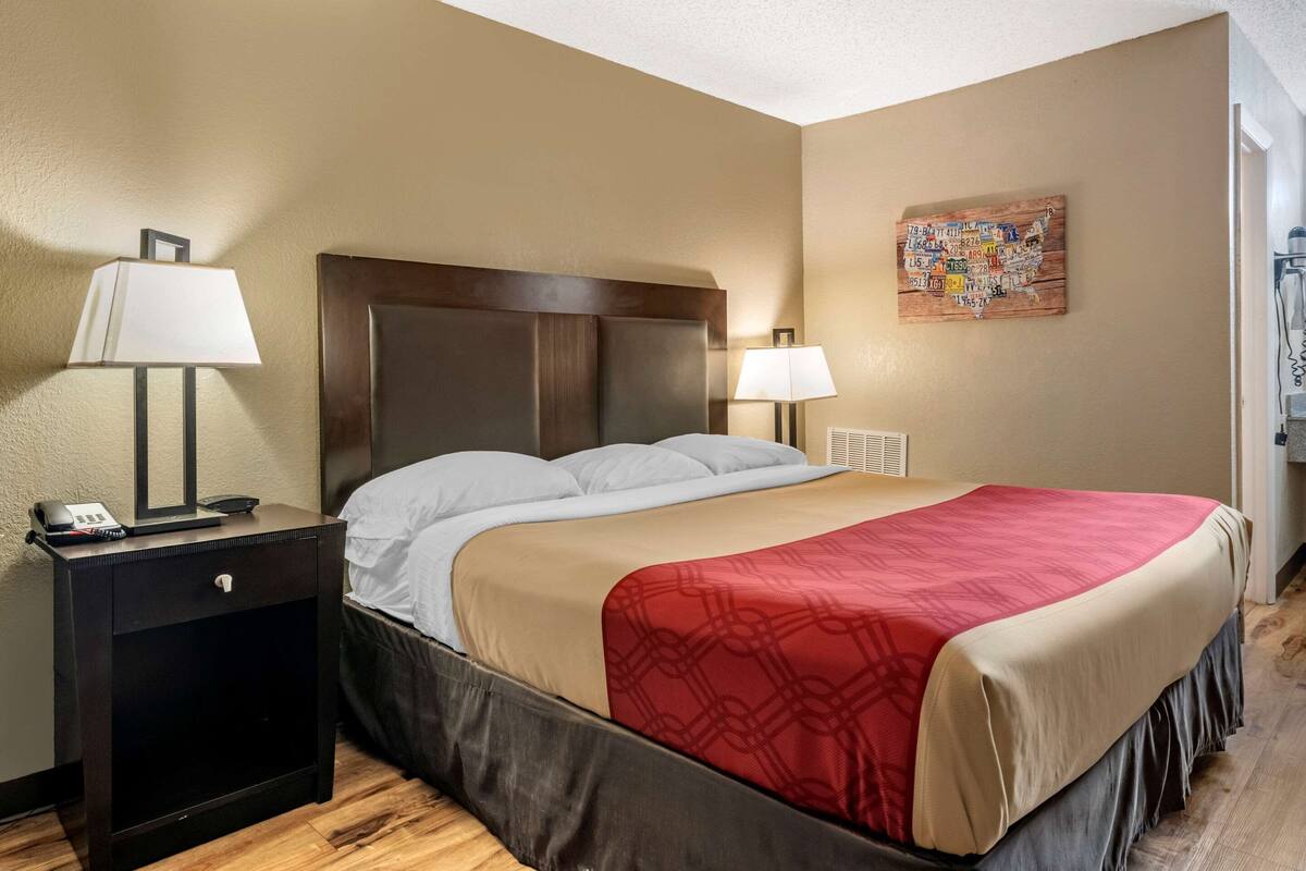 A hotel room with a bed, two bedside tables, a nightstand, a lamp, a wall map, and a thermostat.
