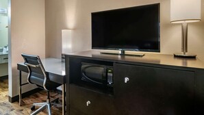 A hotel room with a flat-screen TV, a desk with a chair, a microwave, a lamp, and a minibar. - Econo Lodge Sebring (Avon Park)
