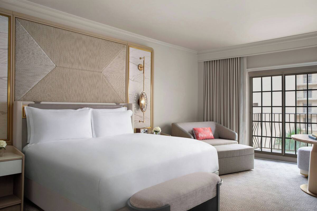 Ein Hotelzimmer mit einem großen Bett, einer Couch, einem kleinen Tisch und Blick auf die Stadt durch große Fenster.
