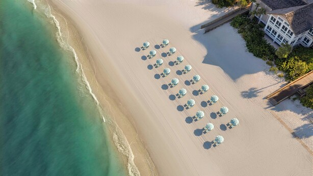 An aerial view of a beach with rows of umbrellas and a building with a sloped roof. - The Ritz-Carlton, Naples (Naples)