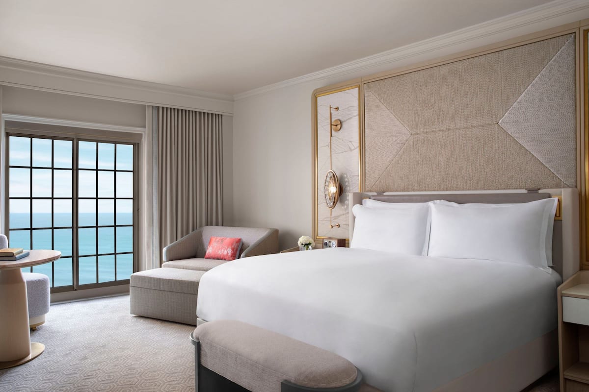 Ein Hotelzimmer mit einem großen Bett, einer Sitzecke mit Meerblick und einem großen Fenster.
