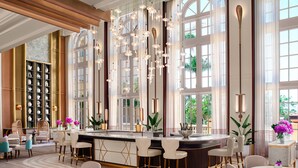A spacious hotel lobby with a central bar area, seating arrangements, and large windows offering views of greenery. - The Ritz-Carlton, Naples (Naples)