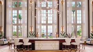A luxurious bar area with a marble countertop, white bar stools, and a large window offering a view of palm trees. - The Ritz-Carlton, Naples (Naples)