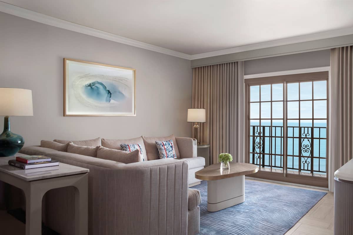 Ein modernes Hotelzimmer mit einer Couch, einem Couchtisch, einer Lampe und einem großen Fenster mit Meerblick.