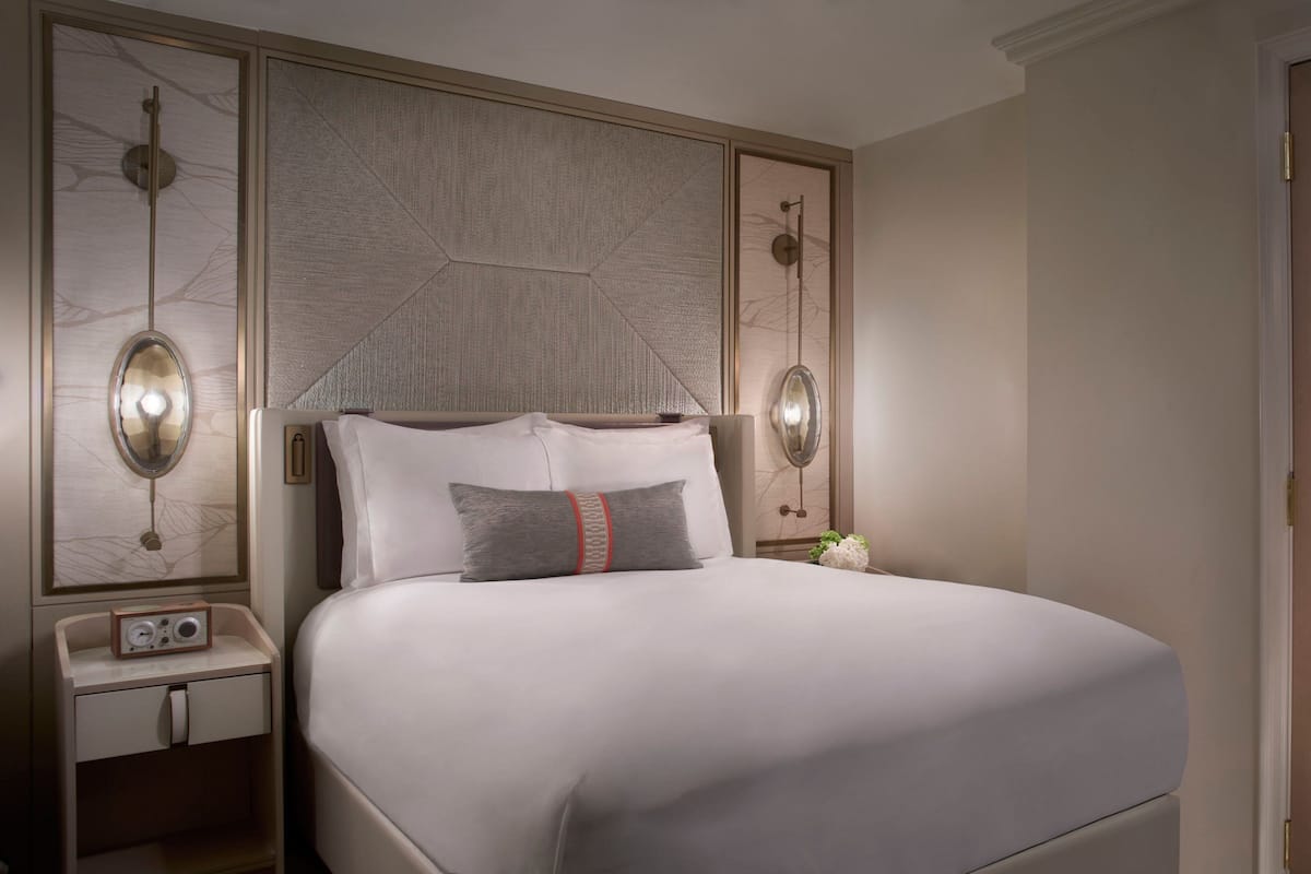 Ein ordentlich eingerichtetes Hotelzimmer mit einem großen Bett, einem Nachttisch mit Radio und einem dekorativen Kopfteil.