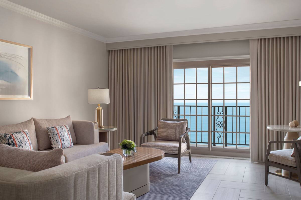 Ein geräumiges Wohnzimmer mit großem Fenster und Meerblick, einem bequemen Sofa, einem Couchtisch und einem Sessel.